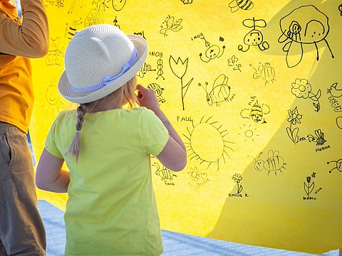 Auf dem Bild sieht man ein Kind, wie es auf ein gelbes Plakat schaut