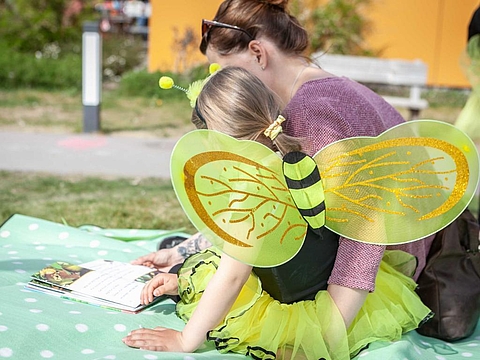 Eine Mutter liest mit einem Kind in einem Bienenbuch